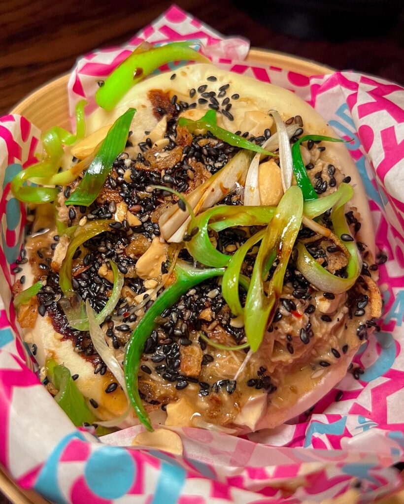 Bao bun in pink and blue paper garnished with scallion and sesame seeds