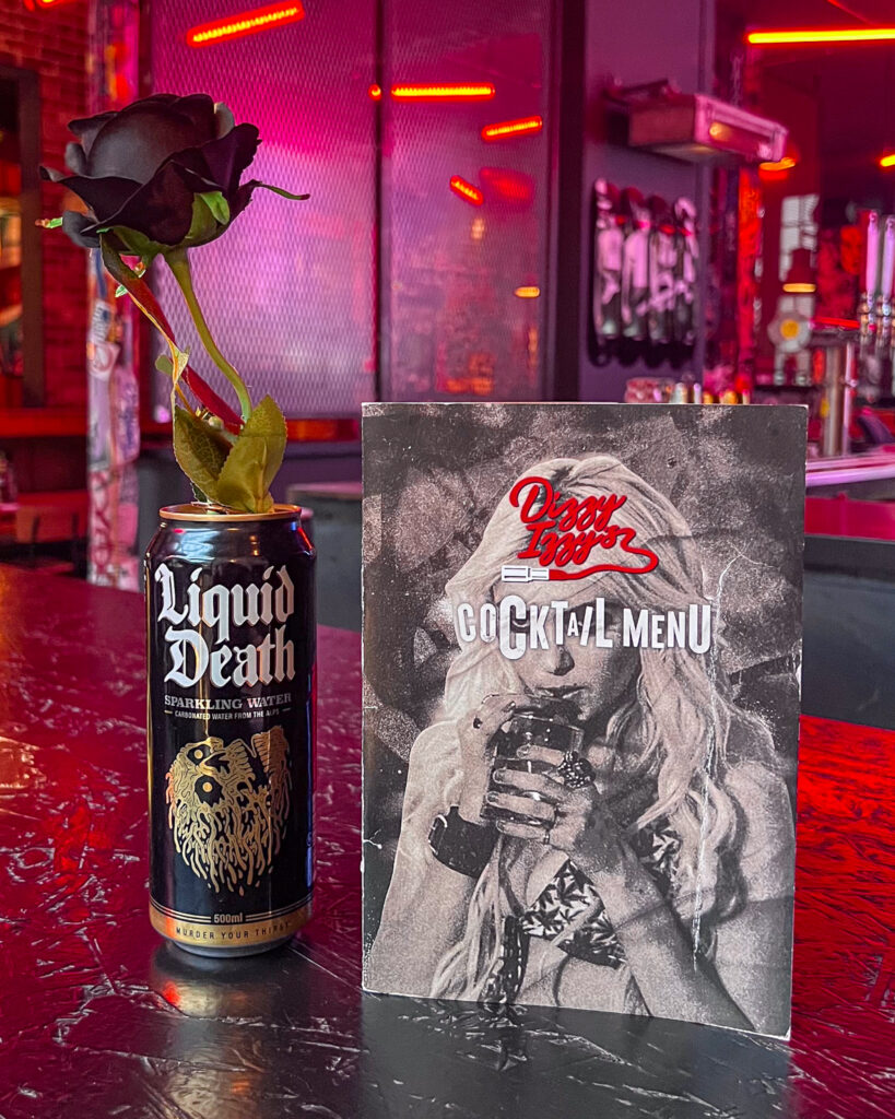 Black can with black rose for decoration beside Dizzy Izzy's punk-inspired cocktail menu