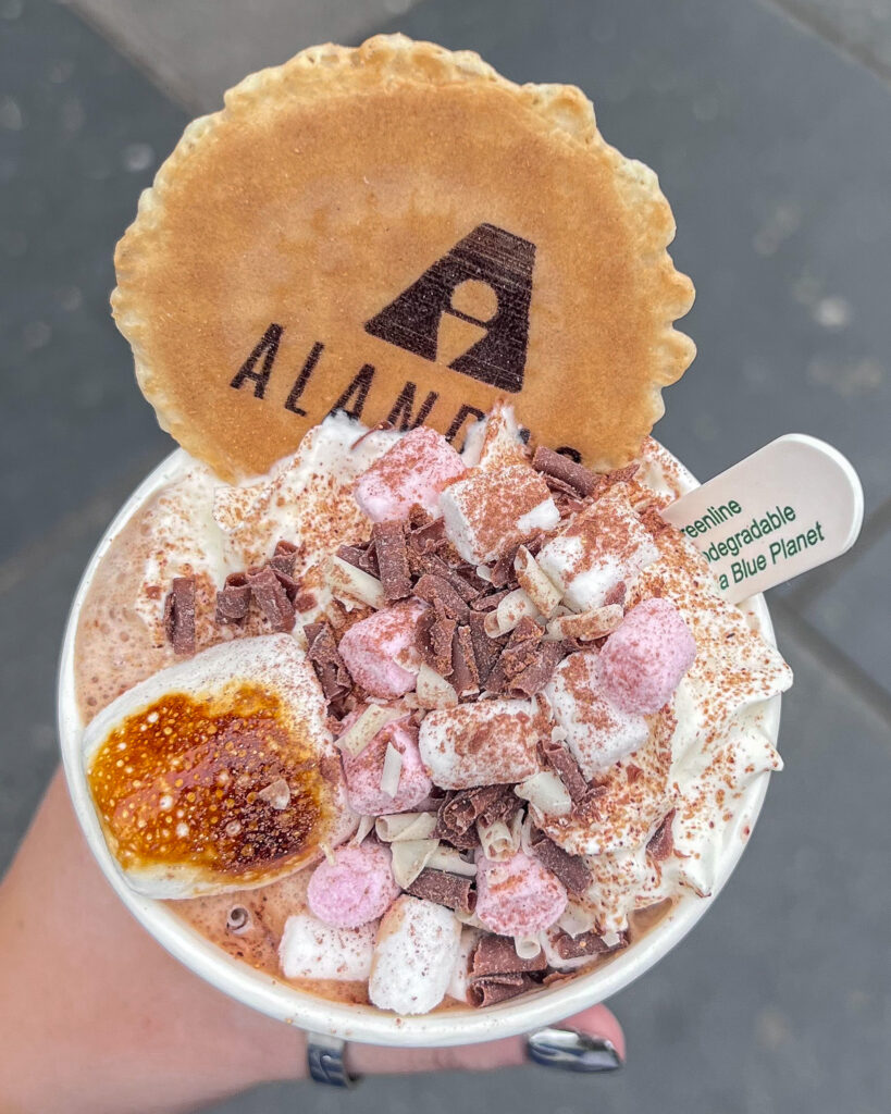 Hot chocolate in black takeaway cup with Alanda's wafer, marshmallows and whipped cream