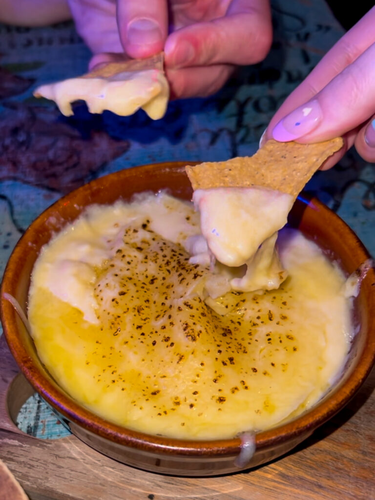 Hands dipping tortilla chips into oozy cheesy queso dip from The Basement