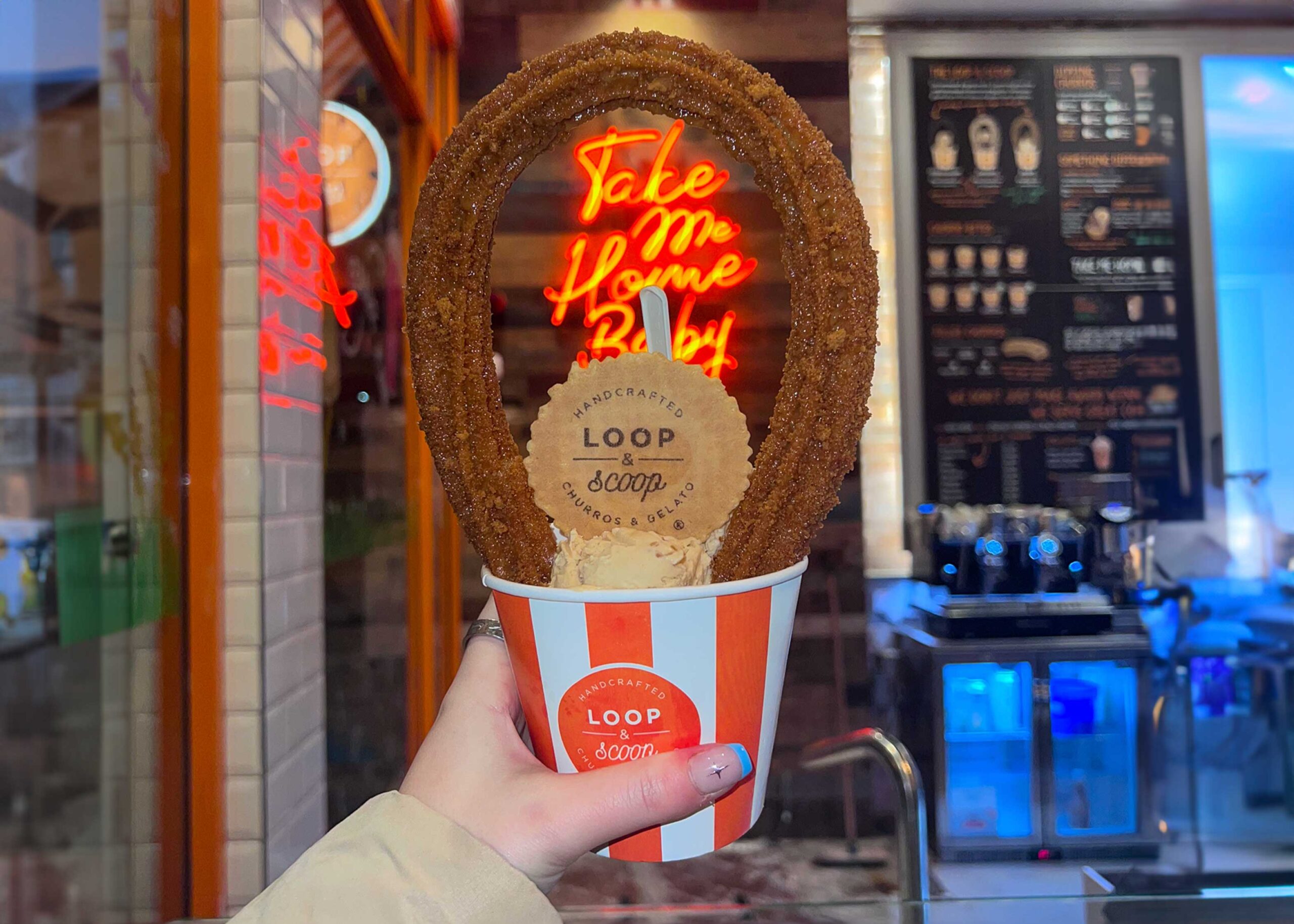Tub of ice cream with a giant looped churro, in front of a neon sign at Loop and Scoop