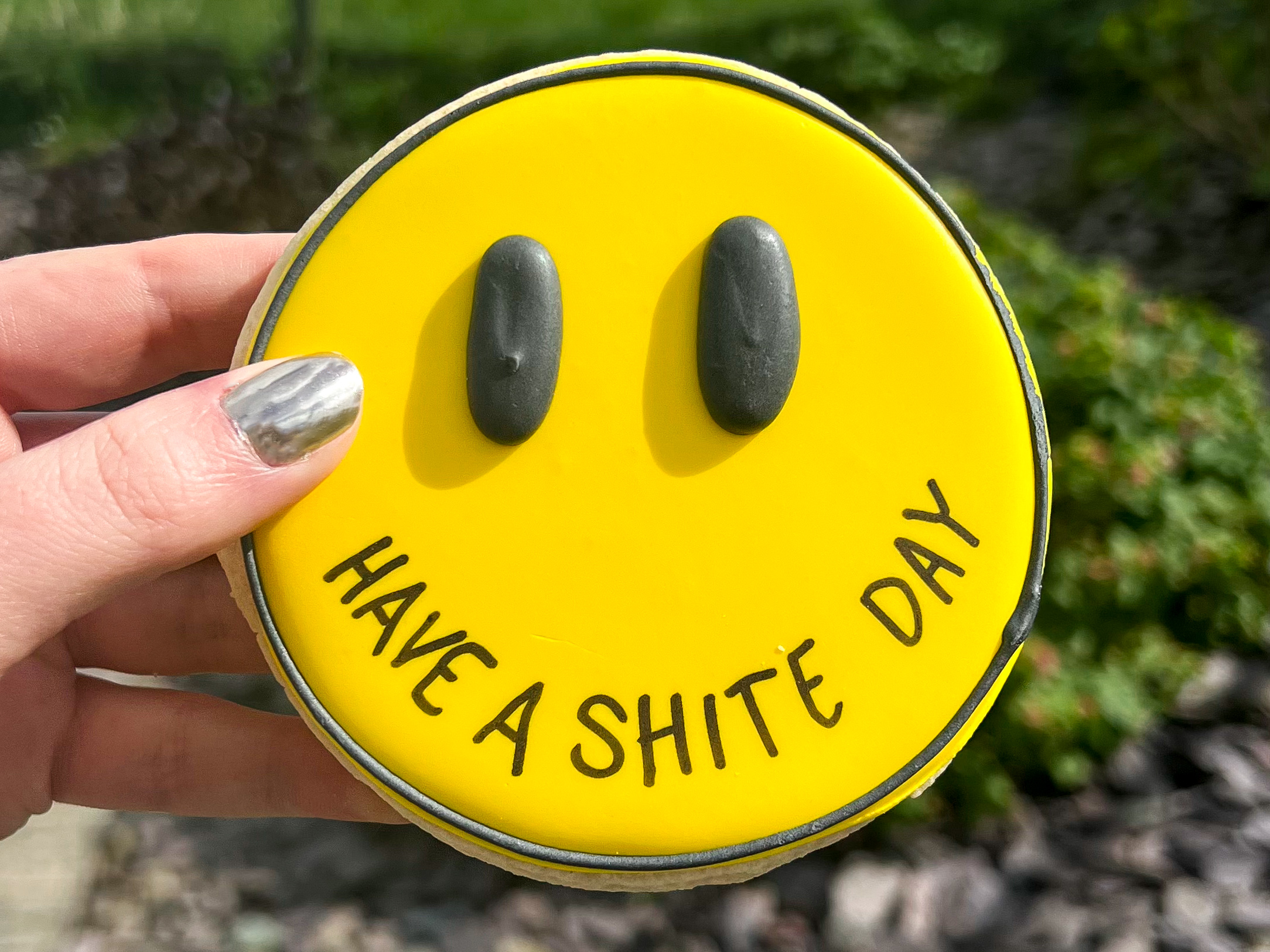Smiley face cookie from Rude Cookies that reads "have a shite day"